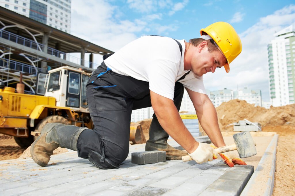Mason worker making sidewalk pavement with stone blocks